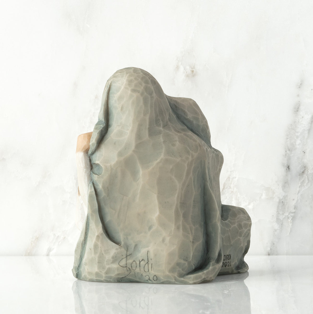 Back view: seated figure with arms around two younger figures, all wrapped in a blue-gray blanket