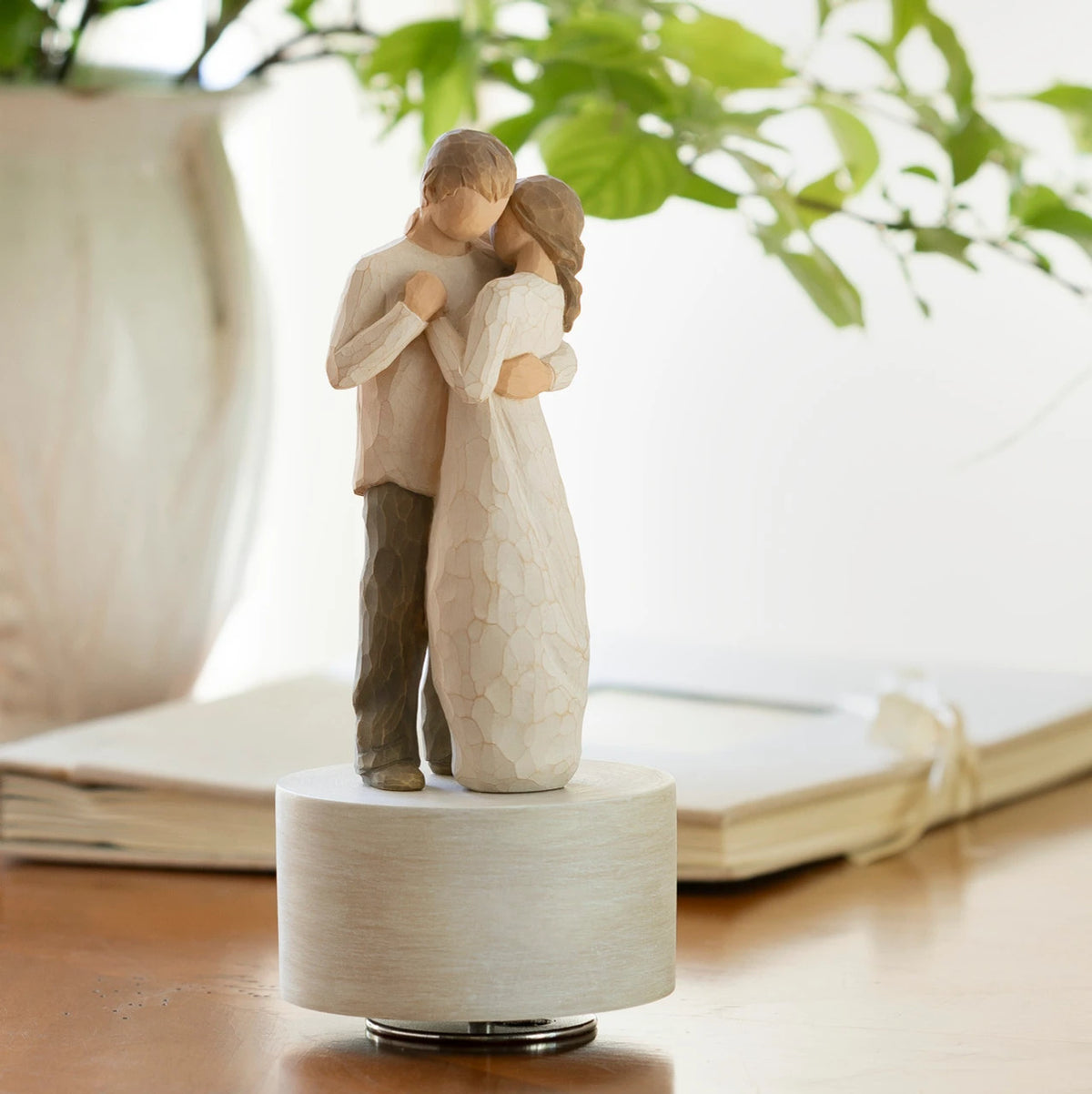 Willow Tree Promise Musical, 8”h hand-painted resin figure of standing couple embracing or dancing, in neutral clothing, atop round, cream base containing musical element, on table near bright window