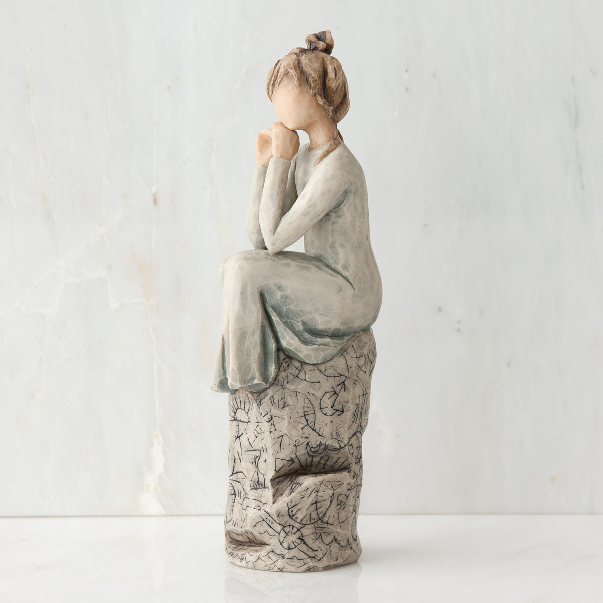 Brunette girl figurine in light grey dress sitting on grey rock facing the side - white background