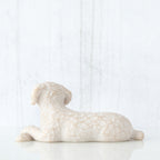 Figure of small white dog laying down with paws crossed in front, facing back