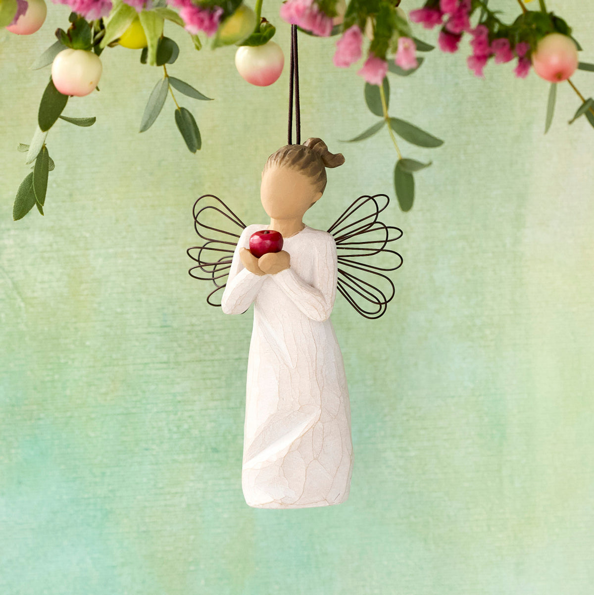 Willow Tree You're the Best! Ornament, 4.5"h hand-painted resin figure in cream dress with wire wings, holding red apple, brown elastic cord, hanging in front of yellow-green painting