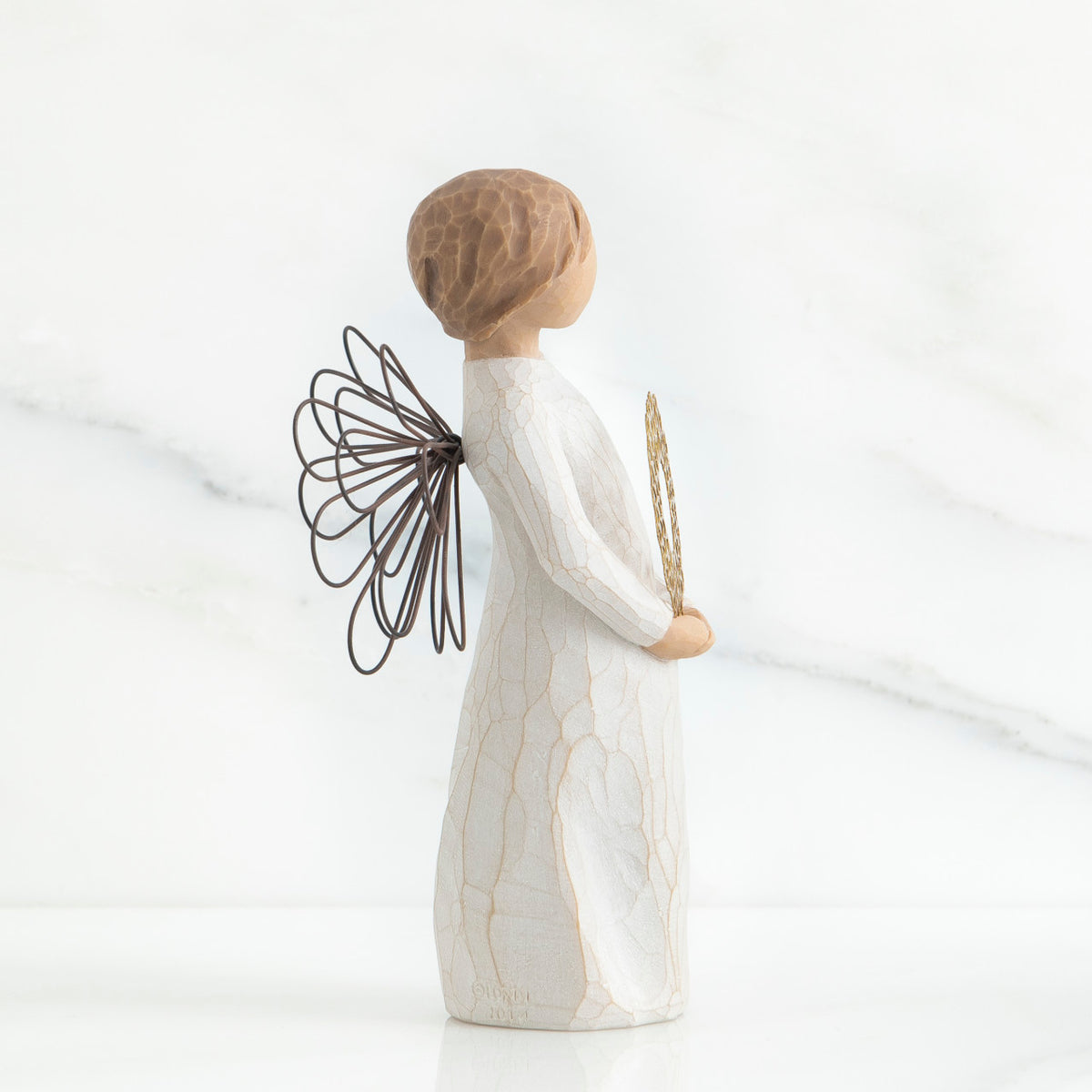 Left side view of angel with short, light brown hair holding a metallic wreath of hearts with both hands