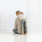 Back view of little boy figurine in blue jeans and white shirt hugging a larger father figurine