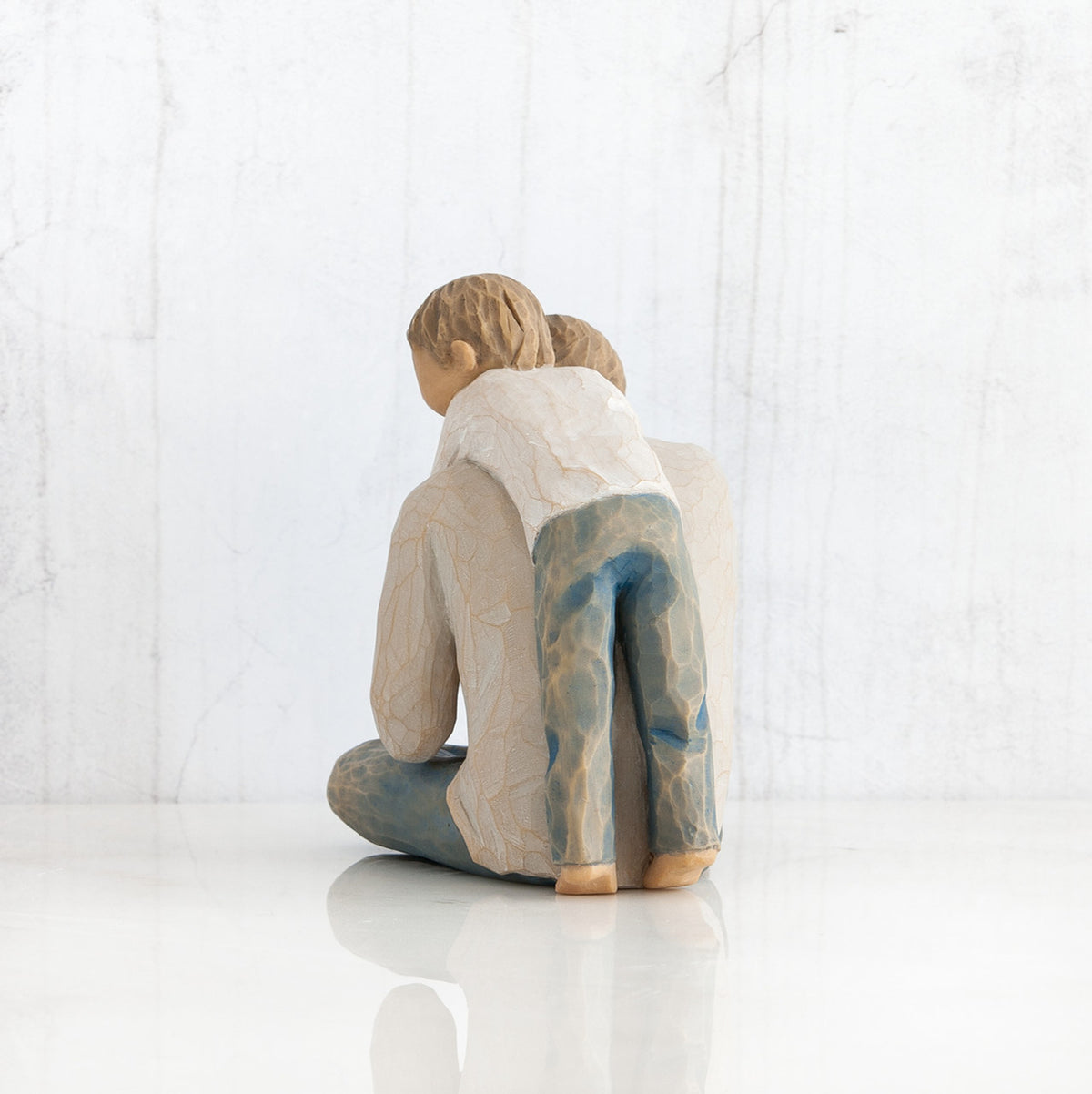 Back view of little boy figurine in blue jeans and white shirt hugging a larger father figurine