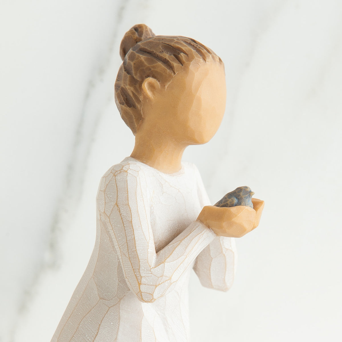Left side close up view of woman with brown hair in a high ponytail leans forward as she holds a gray bird to her chest with both hands
