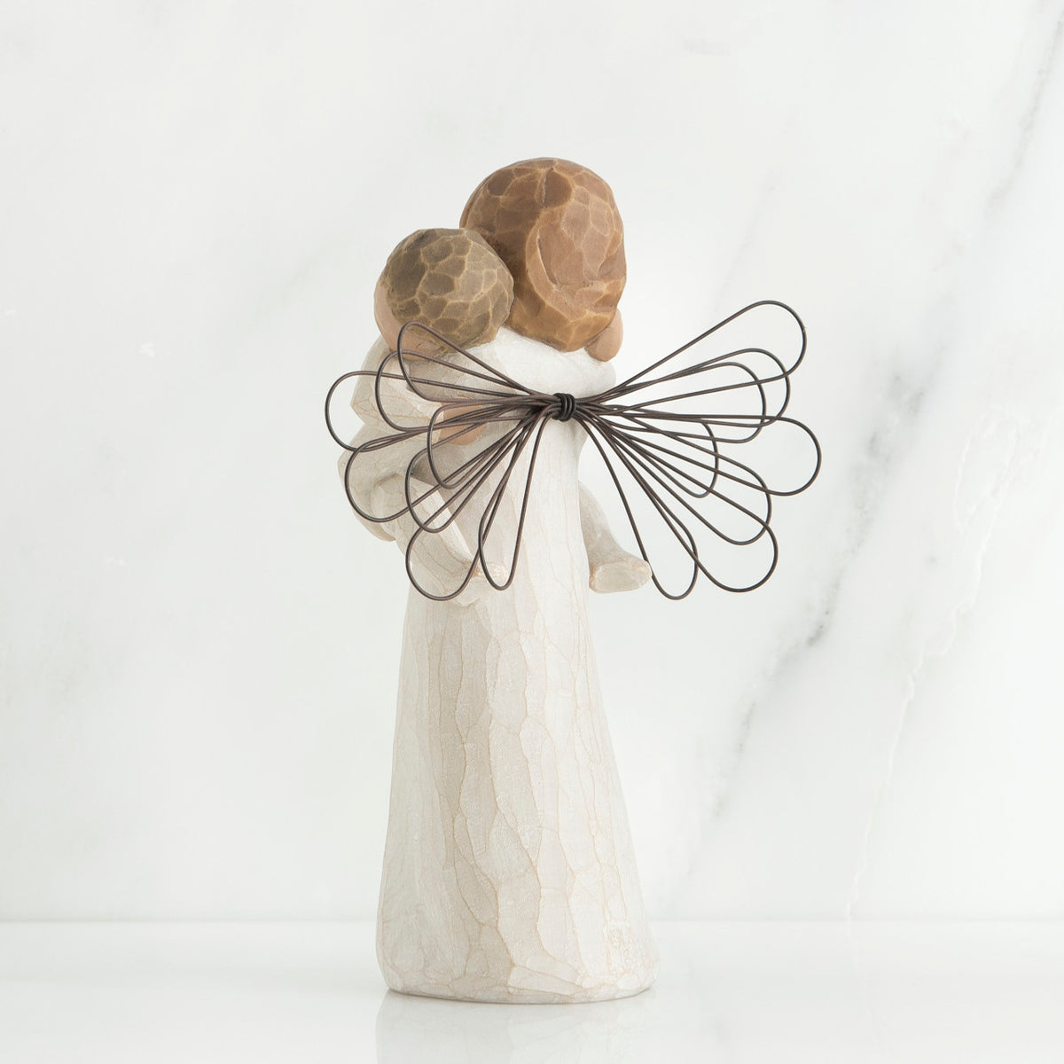 Back view of brunette girl figurine in white dress with brown wings holding baby