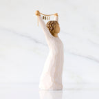 Willow Tree Courage 2025, side view of 6”h hand-painted standing figure in cream dress holding aloft a gold chain with 2025 etched on gold medallions