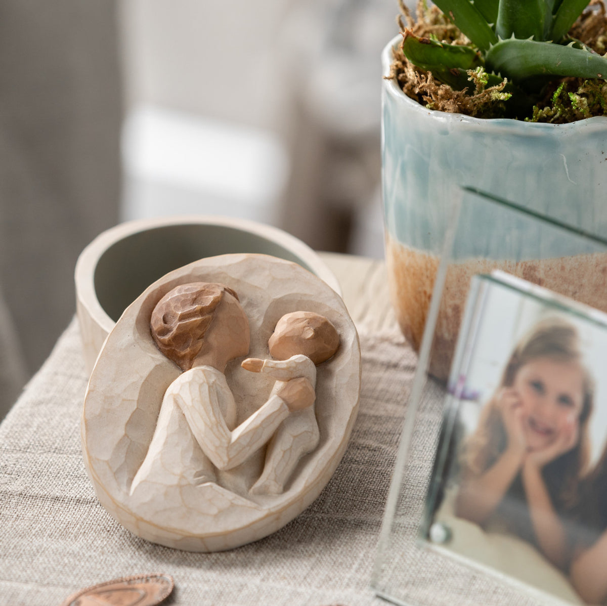 Willow Tree Grandmother Keepsake Box, 3.4" oval x 1.5" h hand-painted resin box with removable lid off to one side. Lid has bas-relief carving of older woman in cream dress, holding up baby, inside of box has sentiment