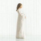Side view of brunette girl figurine in white dress holding her stomach