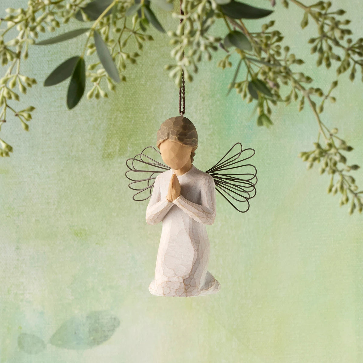 Willow Tree Angel of Prayer Ornament, 3"h hand-painted kneeling resin figure in cream dress with wire wings, hands in prayer position, brown elastic cord, hanging in front of green painting