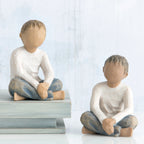 Two young boy figurines sitting next to one another in white shirts and blue jeans