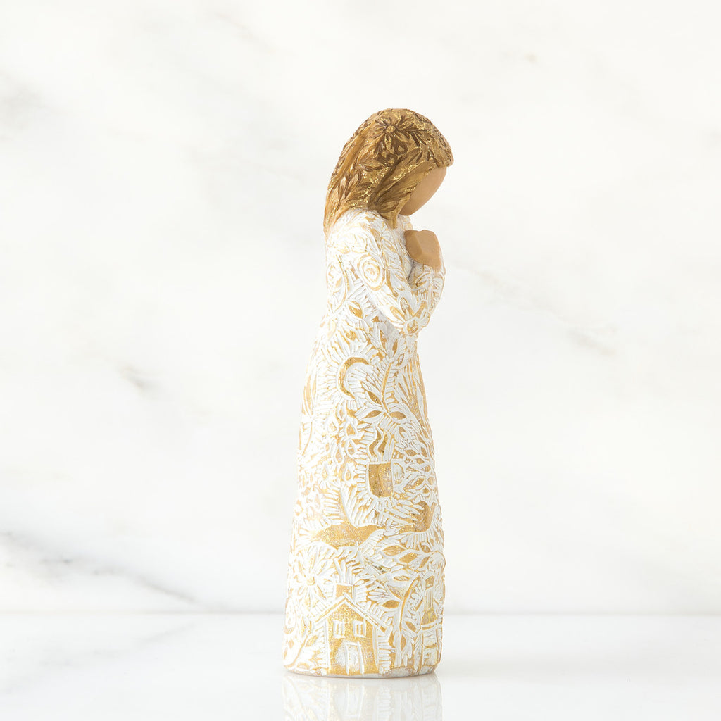 Gold haired girl figurine in white / gold dress facing the side holding her hands to her chest - white background