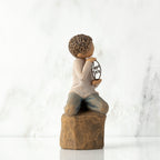 Right view: Figure of lighter-skin child, kneeling on rock, holding wire circle with ‘love you’ written in wire