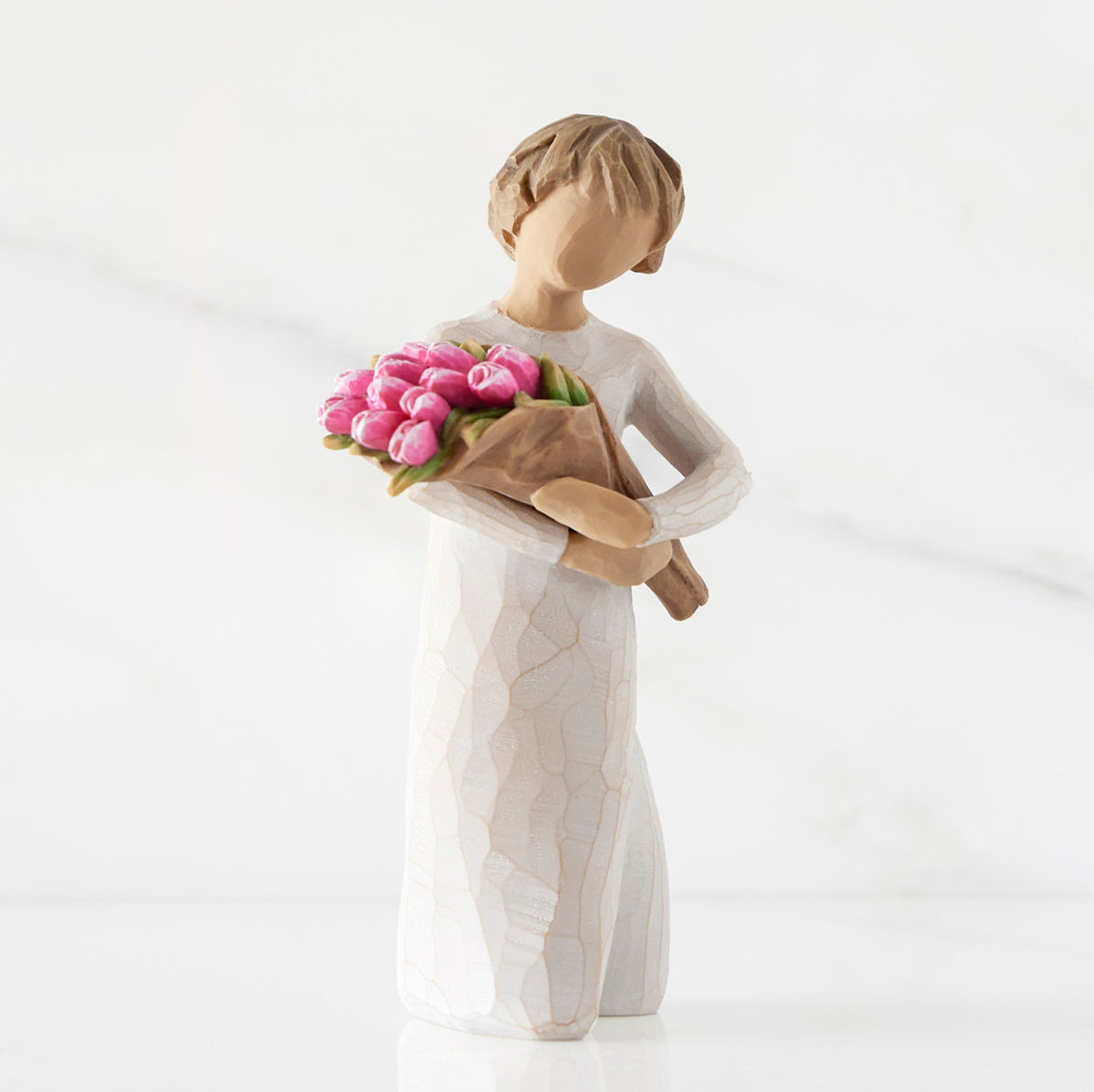 Right side of standing figure in cream dress holding bouquet of pink tulips