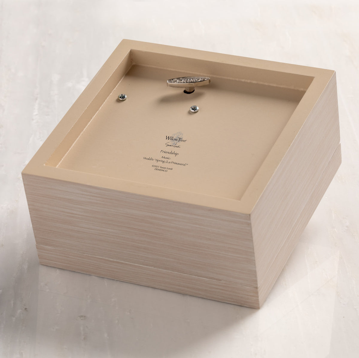 Bottom of cream wood box with hinged lid, showing winding mechanism for music.