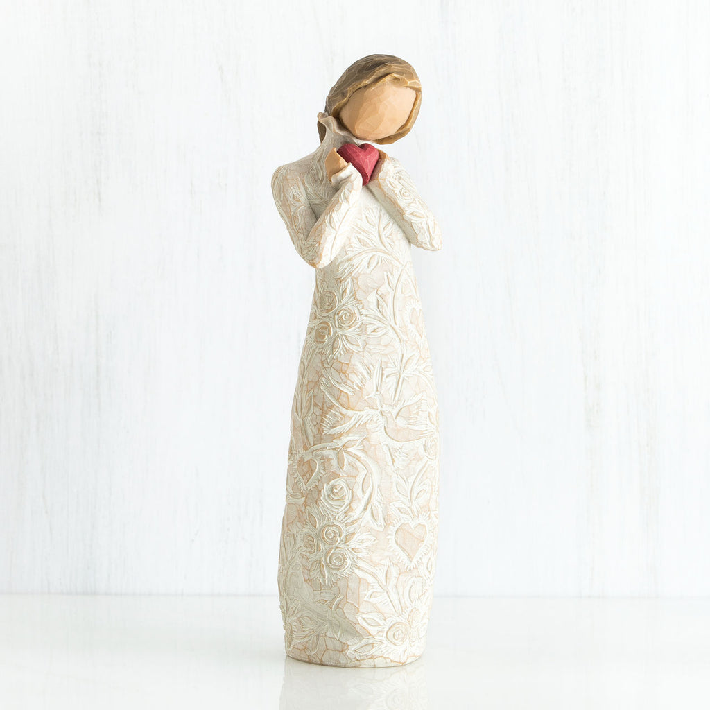 Standing faceless woman figurine in white dress facing forward holding pink heart