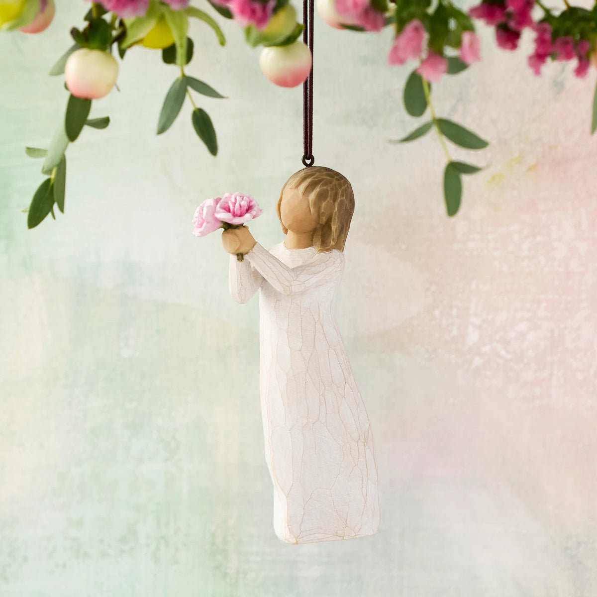 Willow Tree Thank You Ornament, 4”h hand-painted resin figure in cream dress, holding out bouquet of pink peonies, brown elastic cord, hanging in front of pastel painting