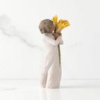 Right side of standing figure in cream dress with darker skin holding yellow calla lilies in her arms