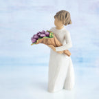 Willow Tree Surprise, 5”h hand-painted standing resin figure in cream dress, holding bouquet of purple tulips, in front of light blue painting