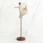 Brunette angel figurine in white dress on wooden stand with her arms out