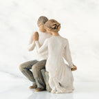Man and woman figurines in white sitting holding hands facing one another
