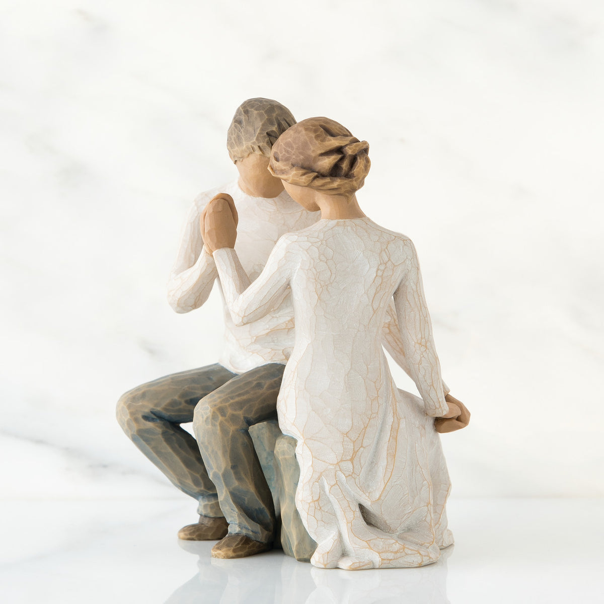 Man and woman figurines in white sitting holding hands facing one another