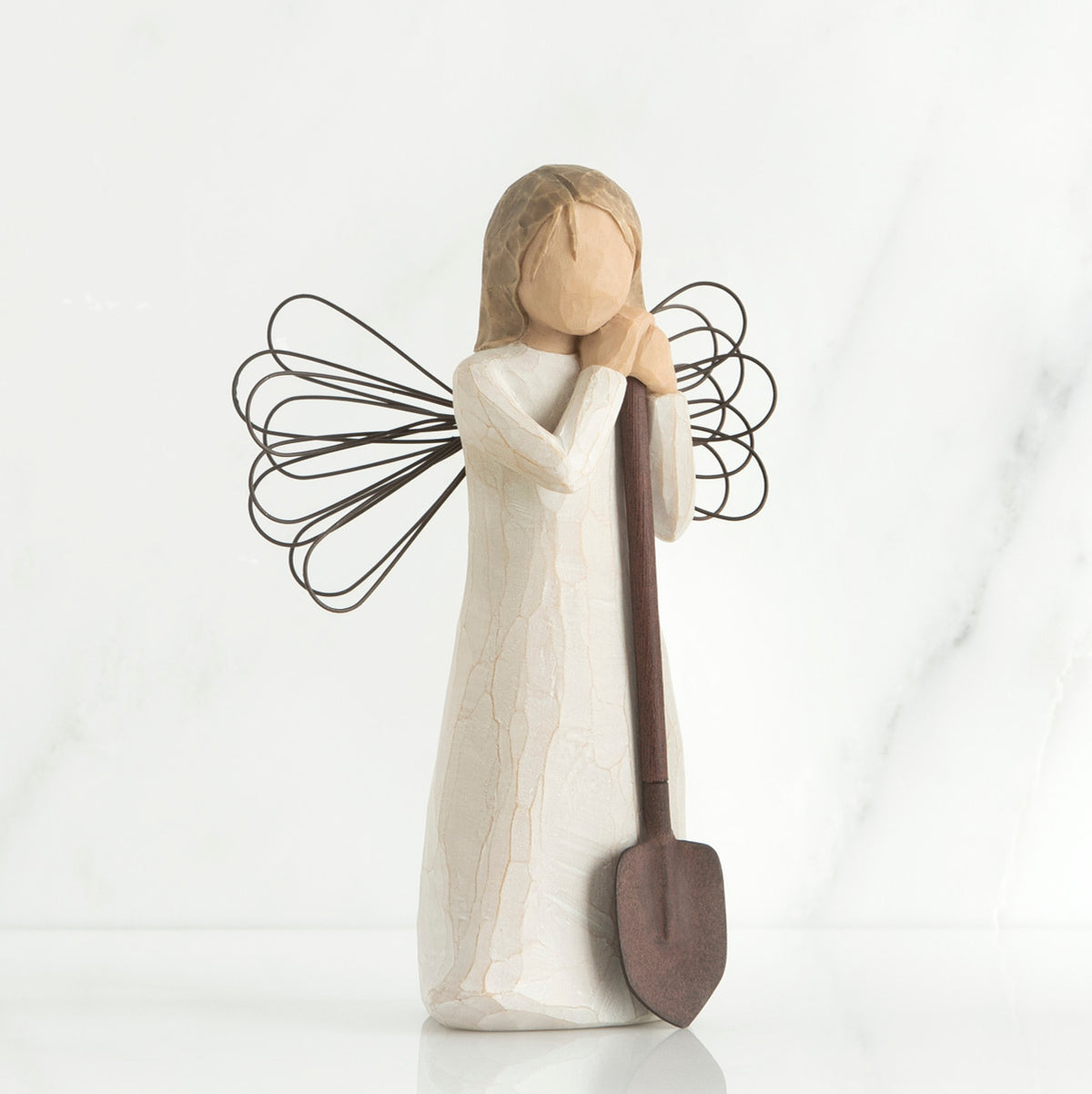 Young faceless girl figurine in white dress with black wire wings holding brown shovel