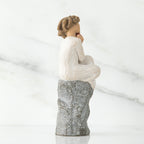 Back view of brunette girl figurine in white dress sitting on grey rock