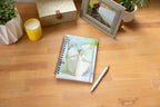 Willow Tree Butterfly Notebook, 6.5"w x 8.5"h, hard-cover, spiral-bound, 240 lined pages, front cover features Butterfly figure on background of blue-green painting, closed on desk