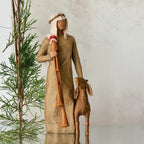 Wiseman figurine in tan dress next to golden lamb figurine with green tree in the background