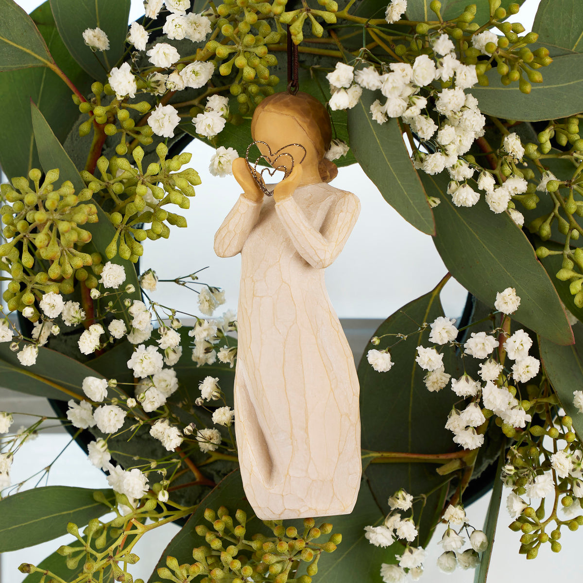 Willow Tree Lots of Love Ornament, 4.5”h hand-painted resin figure in cream dress, holding wire concentric heart with gold glitter, brown elastic cord, hanging in spring wreath
