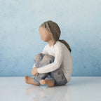 Brunette girl figurine sitting in white shirt and blue jeans with her arms folded on her legs - blue background