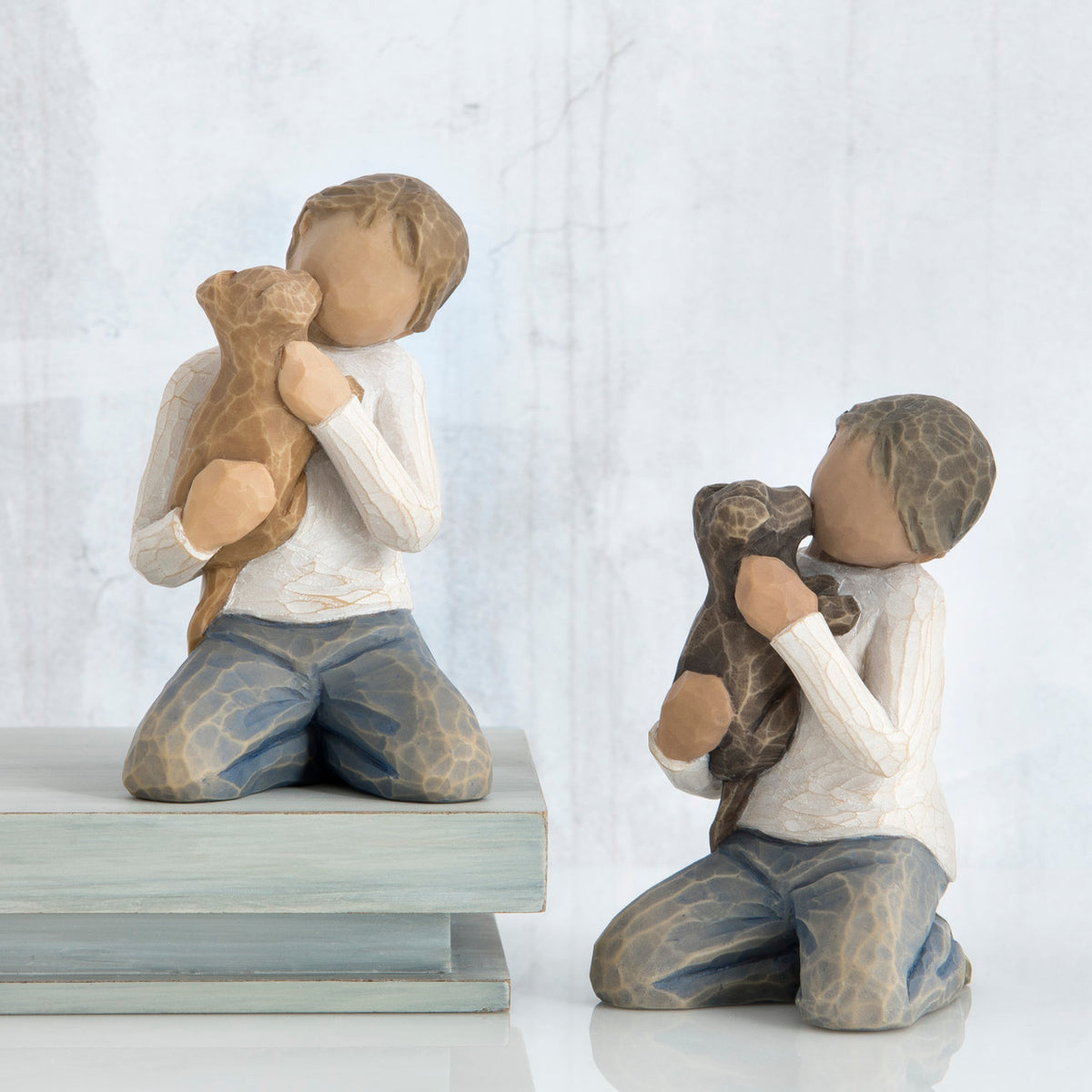 Set of two boy figurines sitting in blue jeans and white shirts holding puppy figurines