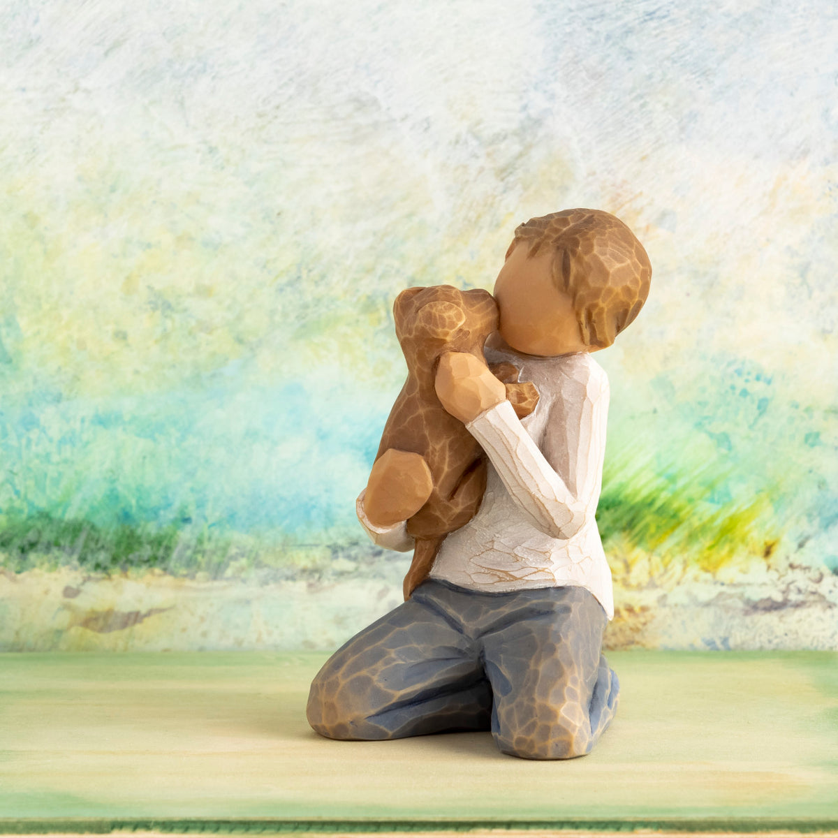 Willow Tree Kindness (boy), 3”h hand-painted resin figure of kneeling boy in neutral clothes holding golden dog, in front of light green painting