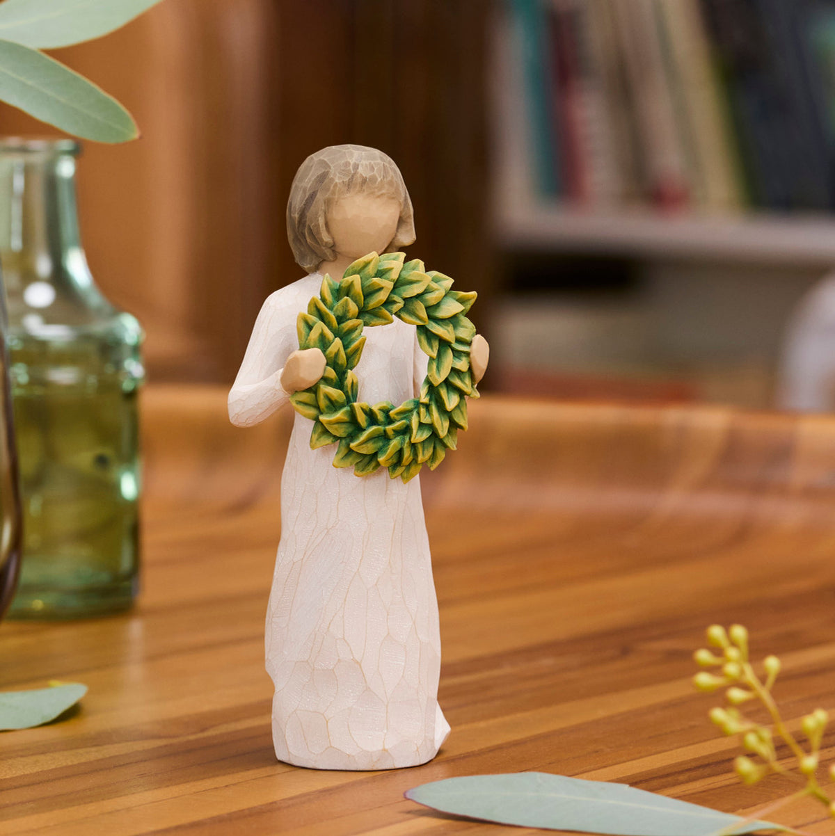 Willow Tree Magnolia, 5.5”h hand-painted standing resin figure in cream dress, holding green magnolia leaf wreath, on wooden desk