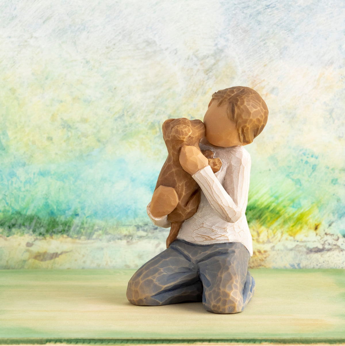 Willow Tree Kindness (boy), 3”h hand-painted resin figure of kneeling boy in neutral clothes holding golden dog, in front of light green painting