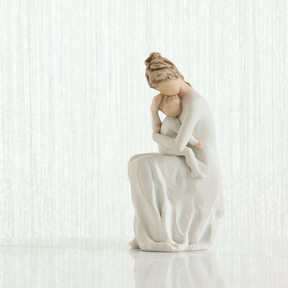 Faceless mother figurine sitting down holding baby - all wearing white and all white background