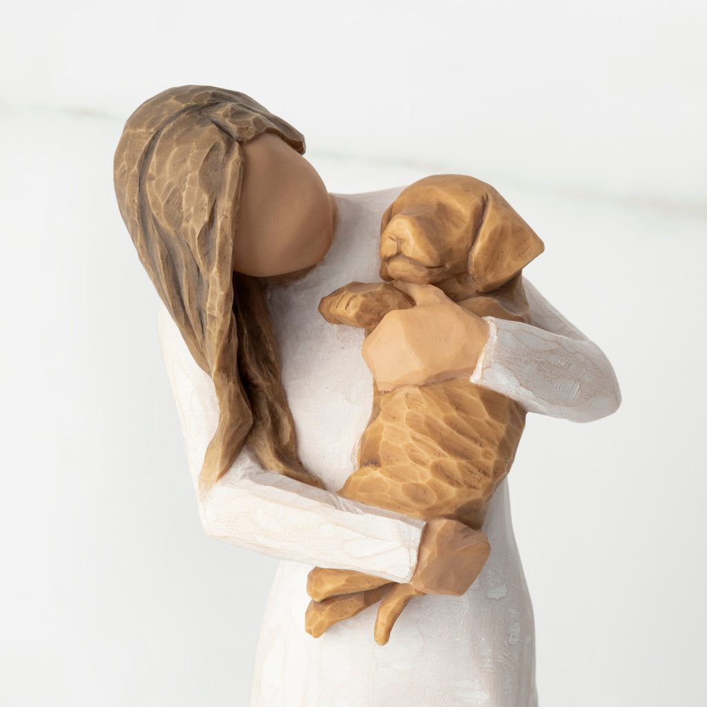 Close-up, cropped view of female figure in cream dress, holding golden color puppy in her arms