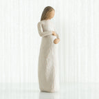 Faceless pregnant woman figurine wearing white dress with hands clutching her stomach