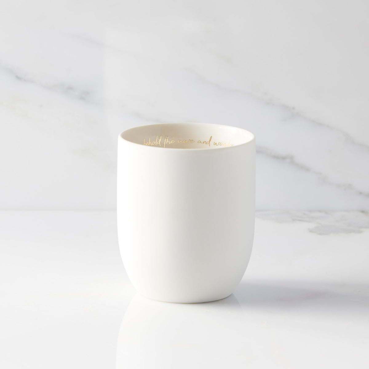 Inside view of unglazed off-white tapered cylinder ceramic candle showing sentiment written in gold along inside rim of vessel