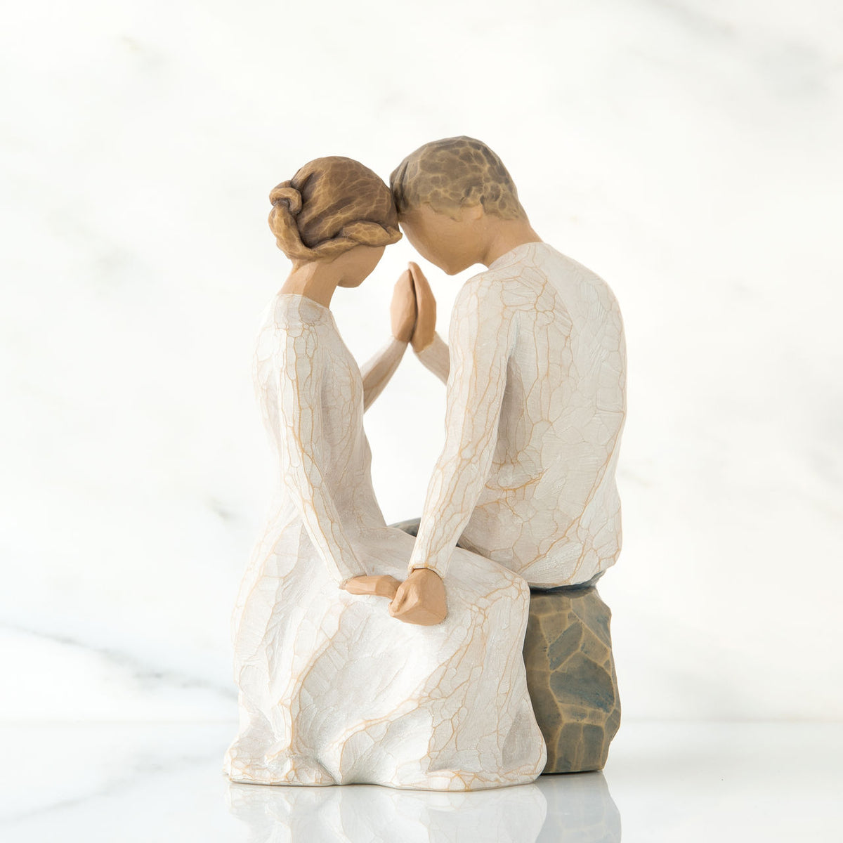 Man and woman figurine dressed in white holding hands facing one another