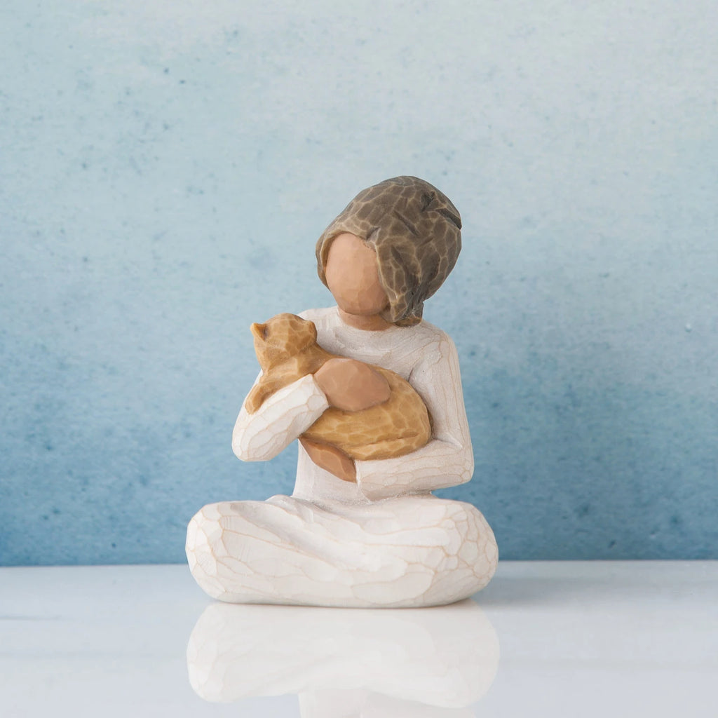 Small faceless girl figurine sitting down holding golden cat in her arms