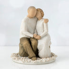 Two faceless figurines - one man and one woman sitting hugging one another on a rock