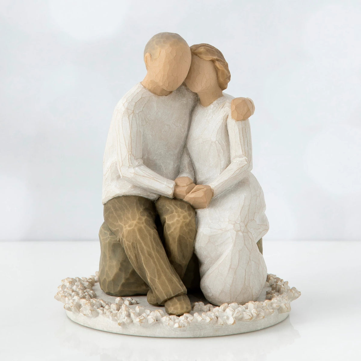 Two faceless figurines - one man and one woman sitting hugging one another on a rock