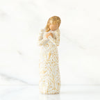 Faceless blonde woman figurine standing in white golden print dress clutching her hands to her chest