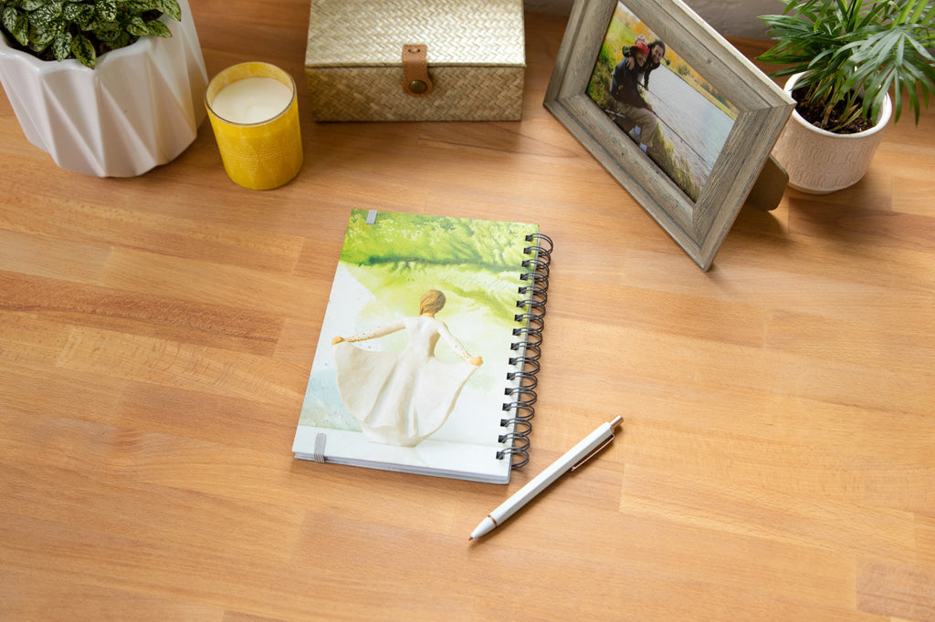 Willow Tree Butterfly Notebook, 6.5"w x 8.5"h, hard-cover, spiral-bound, 240 lined pages, back cover features back of Butterfly figure on background of light green painting, closed on desk