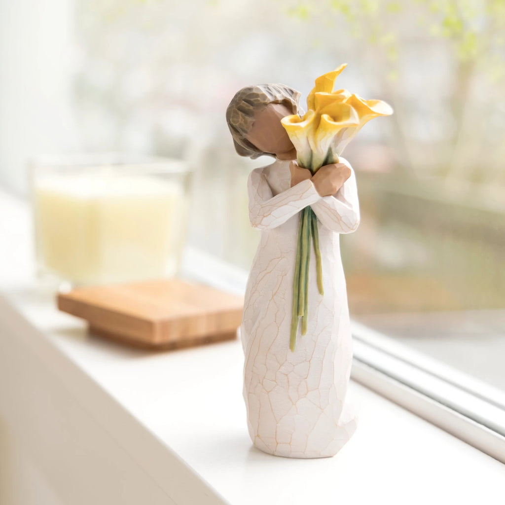 Willow Tree With Gratitude, 5.5”h hand-painted resin figure with darker skin and hair, in cream dress, standing, holding bouquet of yellow calla lilies, on bright windowsill