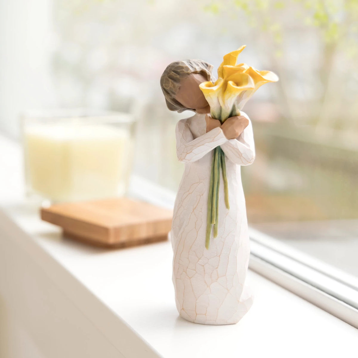 Willow Tree With Gratitude, 5.5”h hand-painted resin figure with darker skin and hair, in cream dress, standing, holding bouquet of yellow calla lilies, on bright windowsill