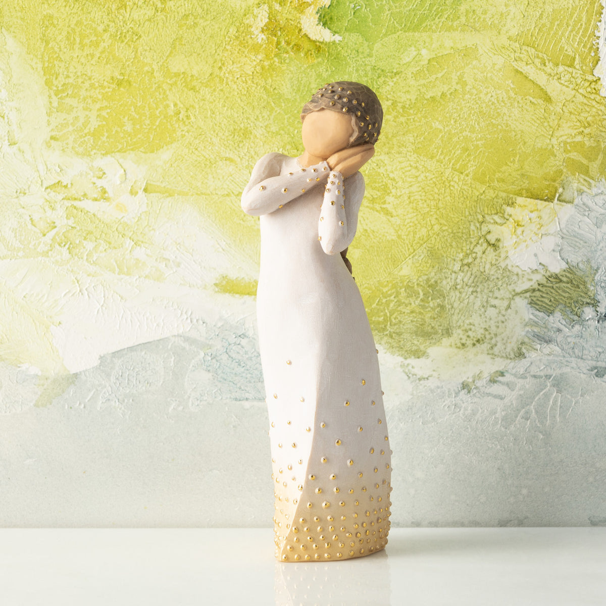 Front view, standing figure in cream dress, holding arms to face in wistful gesture. Hair and dress embellished with gold dots