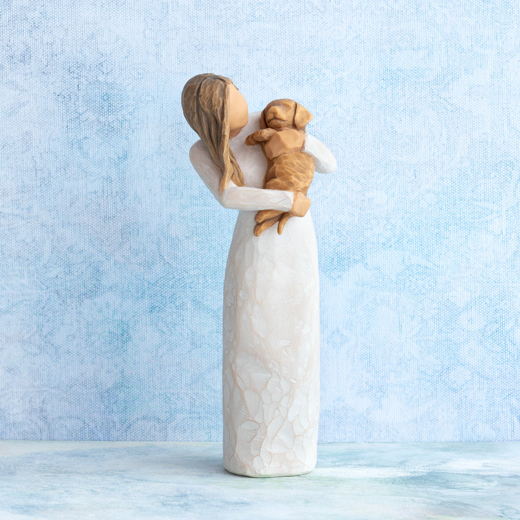 Standing female figure in cream dress, holding golden color puppy in her arms, on blue painted background